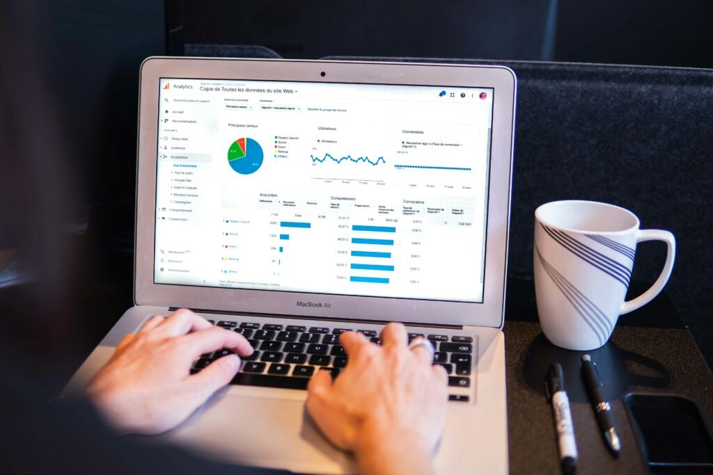 Person typing on a laptop showing a website analytics dashboard with traffic and conversion charts, beside a coffee mug