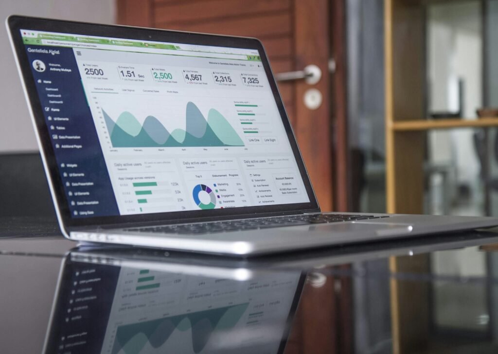 Laptop on a glass desk displaying a website performance dashboard with growth charts, reflected in the desk surface
